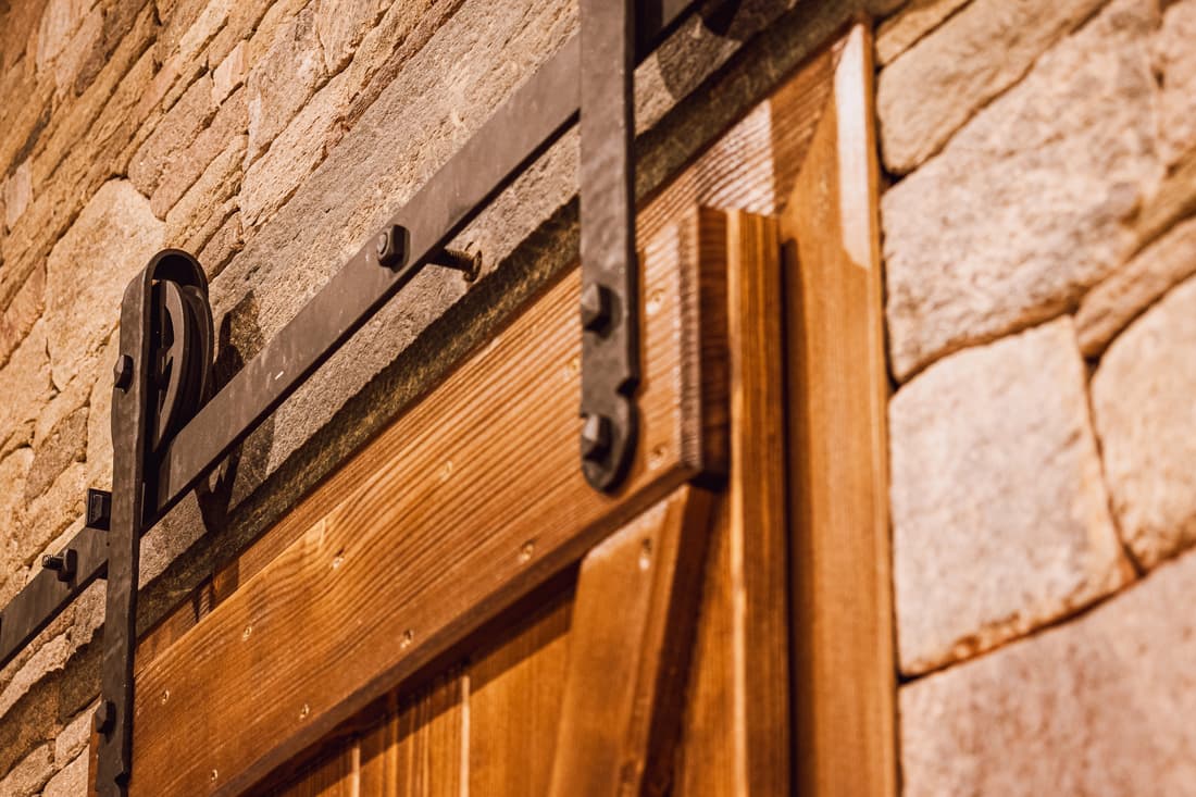 Detailní záběr na černé ocelové kování a pojezd rustikálních dřevěných dveří.