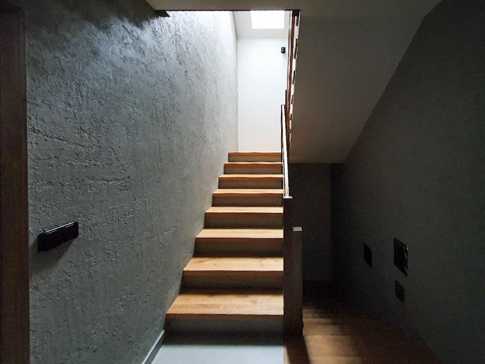 Masivní dřevěné schody vedoucí do horního podlaží chaletového ubytování s tmavým obložením stěn.