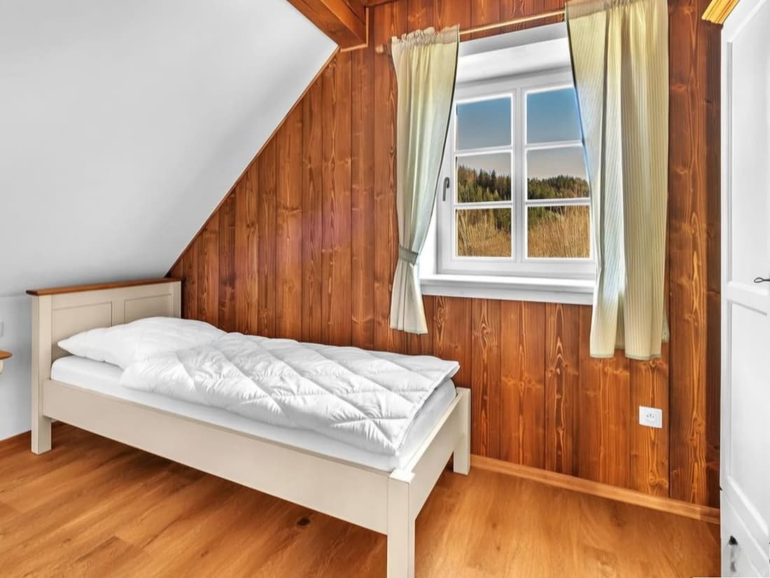 Jednolůžková postel z masivu umístěná u stěny s obložením v útulném podkrovním pokoji chalupy.