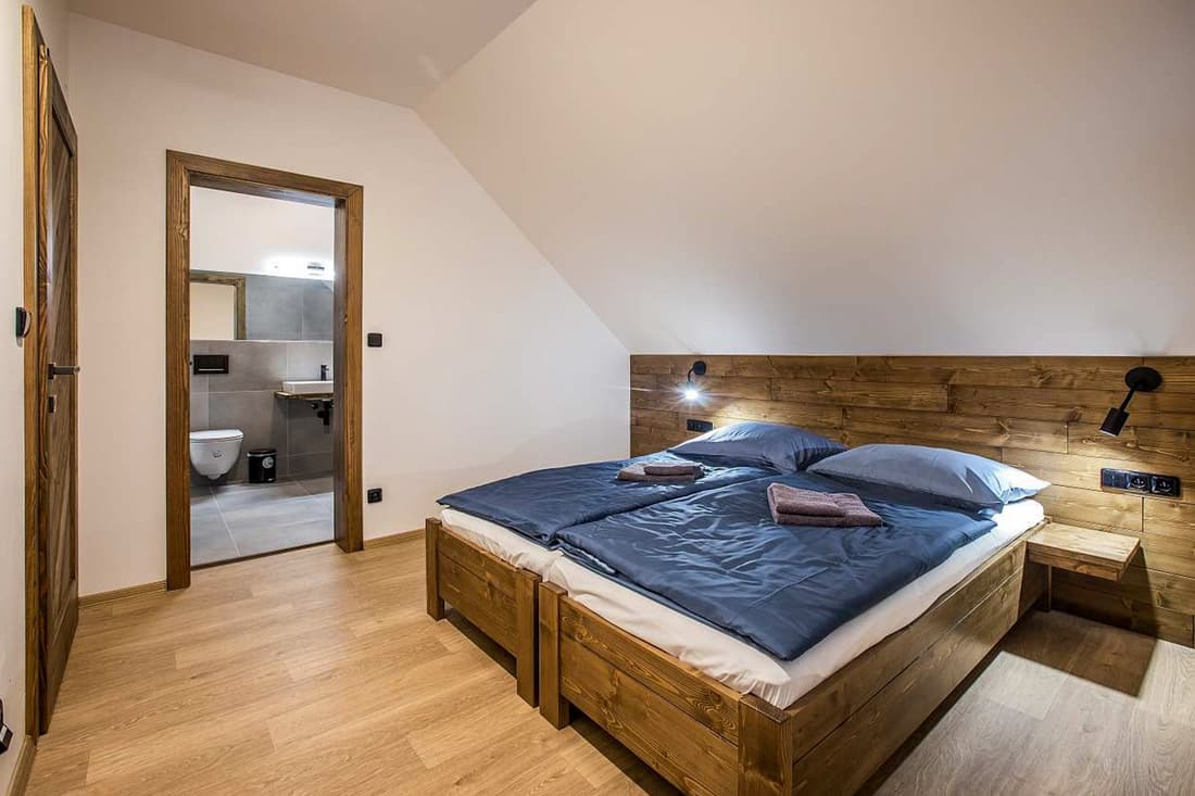 Velká manželská postel z poctivého masivního dřeva s čelem v podkrovním pokoji apartmánu.