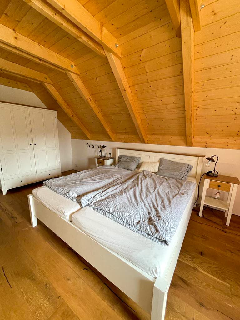 Světlá manželská postel s nočními stolky z masivního dřeva vyrobená na míru do podkrovní ložnice chalupy.