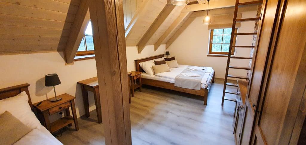 Dvoulůžková postel z poctivého masivu s nočními stolky pod přiznanými krovovými trámy v chaletu.
