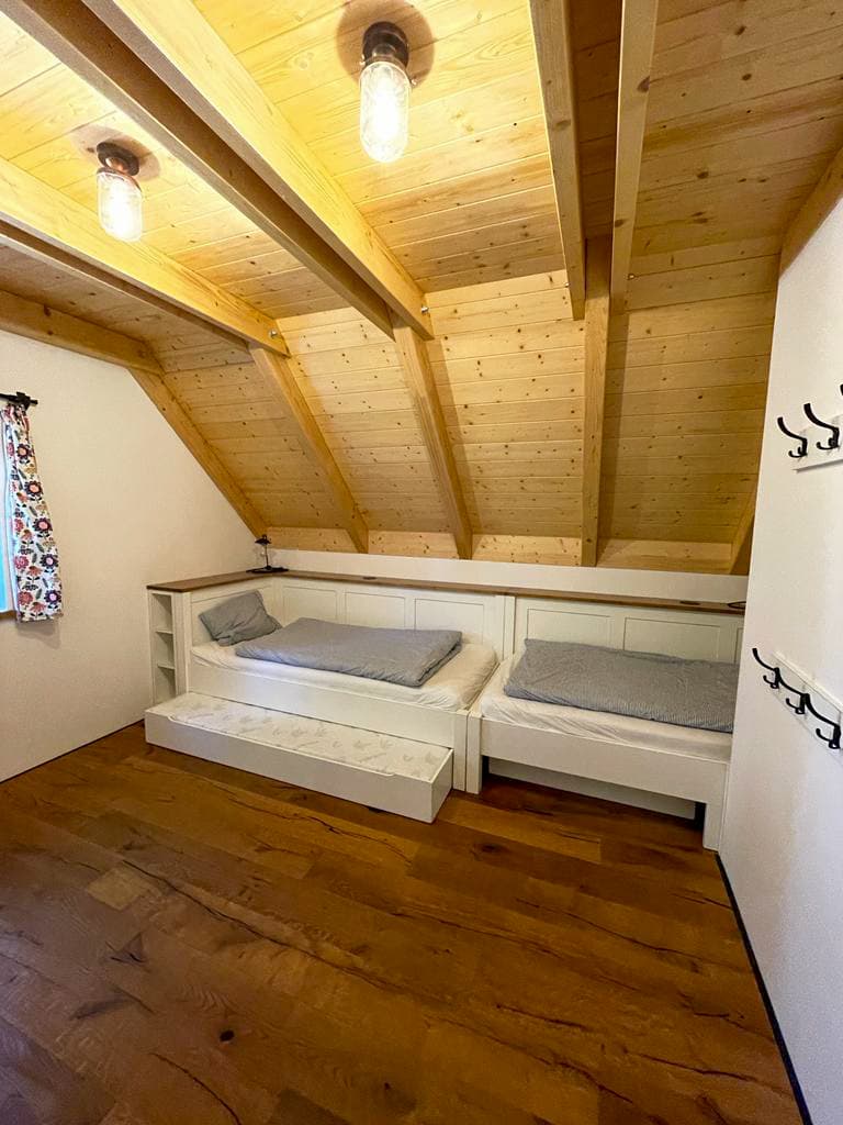 Dřevěné postele na míru z masivu s přistýlkovým výsuvem v podkrovním pokoji pod trámy chalupy.