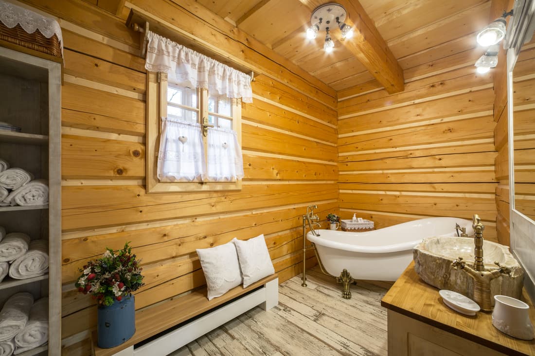 Dřevěná koupelna na chalupě s romantickou vanou, masivní lavicí a skříňkou na ručníky z masivu.