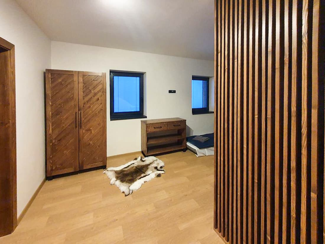 Prostorná chodba s dřevěnými skříněmi, dekorativní lamelovou stěnou a lavicí.