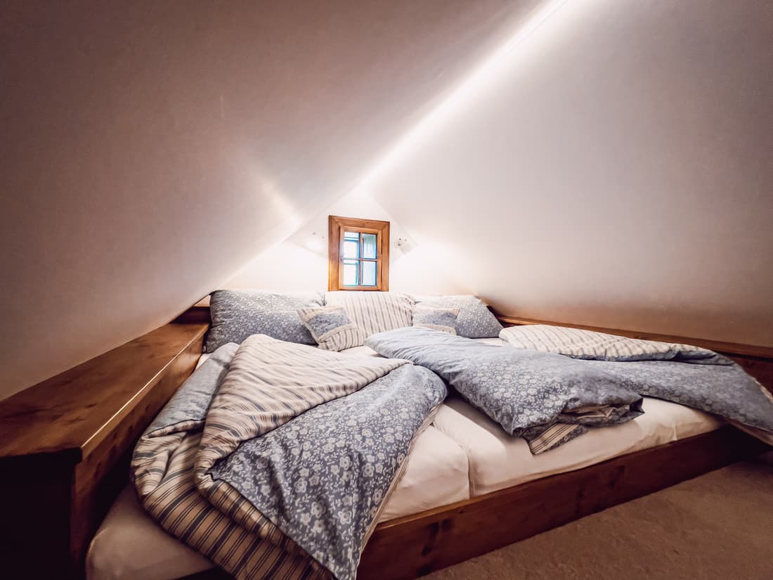 Pohled na podkrovní lůžko z masivu zasazené do útulného prostoru pod střešními trámy.