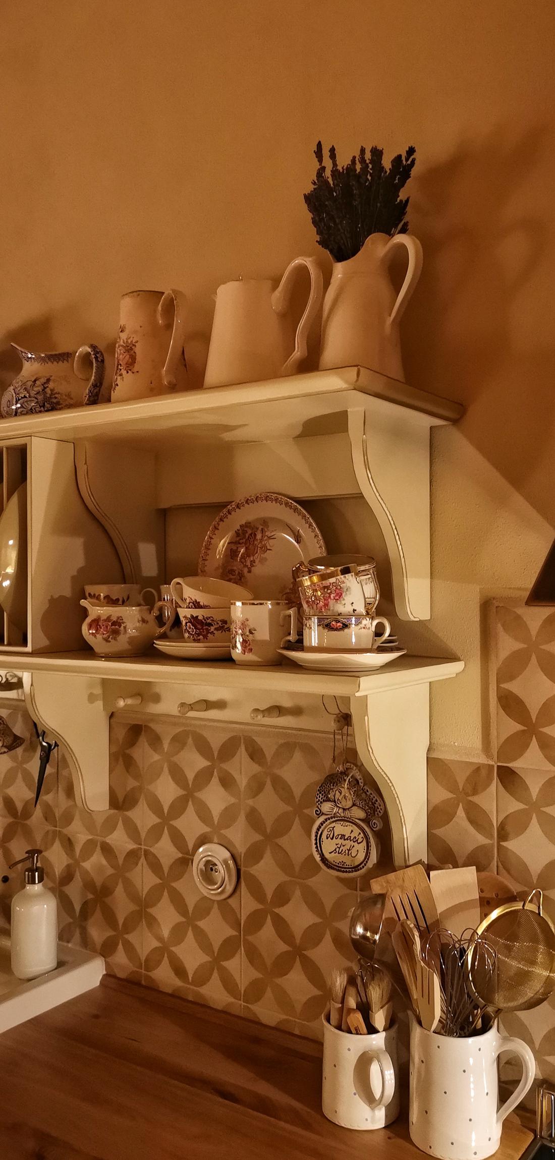 Detail dekorativní vyřezávané police z drásaného masivu ze starých prken nesoucí stylový kuchyňský porcelán a nádobí.