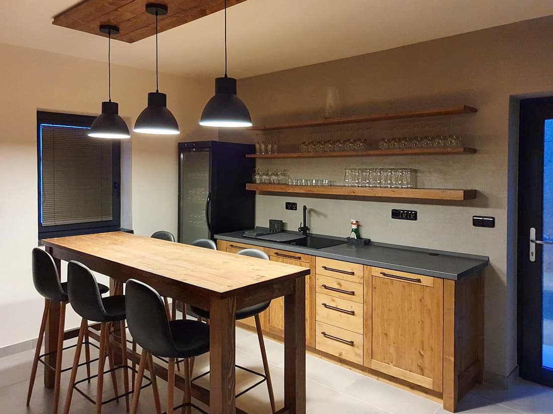 Vysoký barový stůl z masivu s židlemi a stylovým osvětlením v kuchyňské části apartmánu.