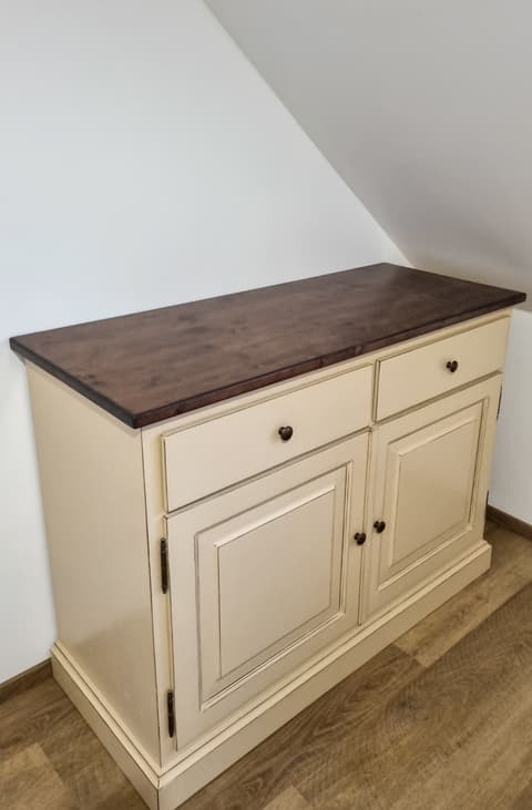 Elegantní bílá komoda z masivu s kontrastní tmavou dřevěnou horní deskou a praktickými dvířky.