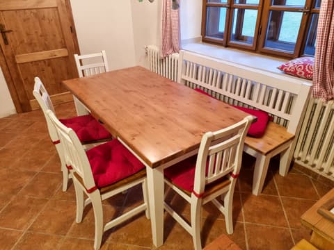 Dřevěná rohová lavice z masivu v bílém provedení s červeným polstrováním, jídelním stolem a židlemi.