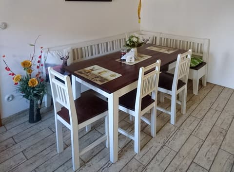 Jídelní kout s rohovou lavicí z masivu v bílé barvě, doplněný stolem s kontrastní tmavou dřevěnou deskou.