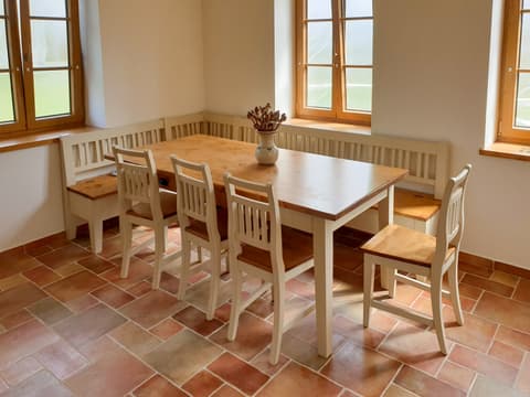 Dřevěný jídelní stůl z masivu s přírodní vrchní deskou a bílou podnoží doplněný rohovou lavicí na chalupě.