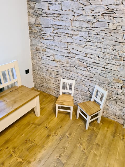 Roztomilé malé dětské židličky z masivního dřeva v bílém provedení stojící na dřevěné podlaze vedle lavice.