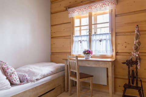 Rustikální psací stolek a židle z masivu umístěné pod oknem s garnýží v podkrovním pokoji.