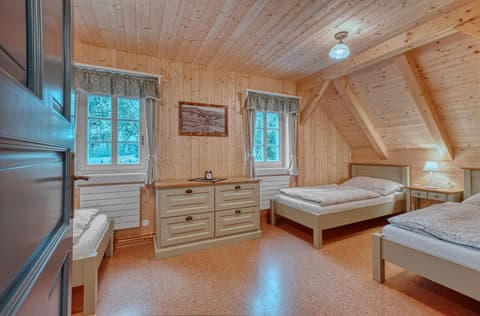 Masivní zásuvková komoda v selském stylu pod oknem v podkrovní ložnici roubenky s jednolůžkovými postelemi.