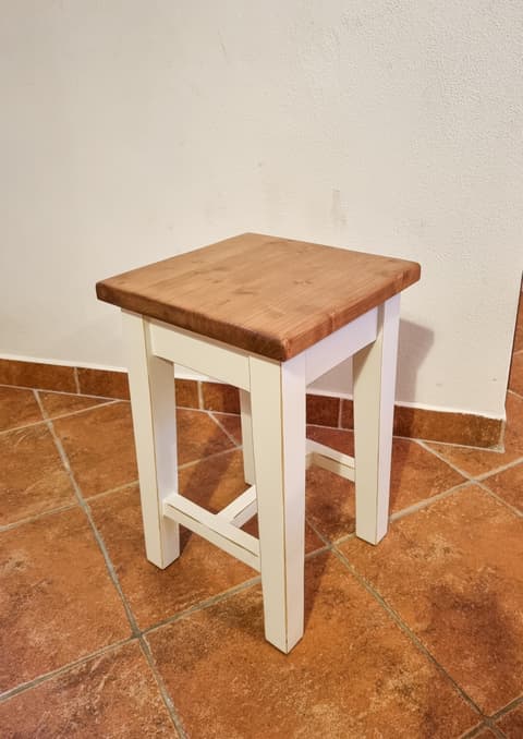Nízká dřevěná stolička neboli taburet z masivu s bíle natřenýma nohama a přírodní horní deskou.