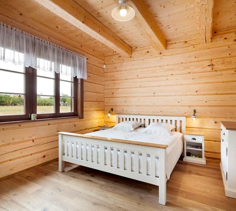 Bílá manželská postel z poctivého masivu s nočními stolky v podkrovní ložnici roubenky.