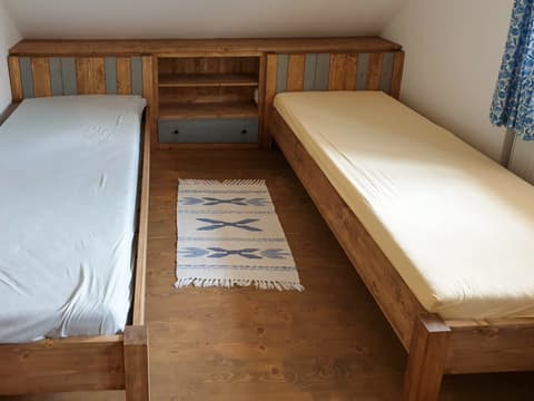 Dvě jednolůžkové postele z masivního dřeva efektivně spojené rohovým stolkem v útulném pokoji s dřevěnou podlahou.