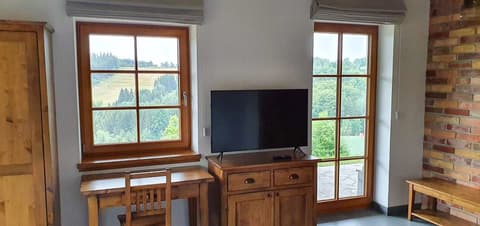 Dřevěná TV komoda a psací stůl z masivu umístěné pod oknem s výhledem v podkrovní ložnici.