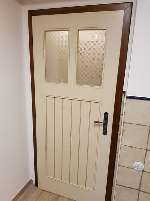 Světlé dveře z masivu do koupelny s horním ornamentálním sklem a spodní svislou dřevěnou profilací.