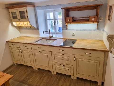 Venkovská kuchyně ze slonově bílého masivu umístěná pod okny chalupy s elegantními mosaznými úchytkami
