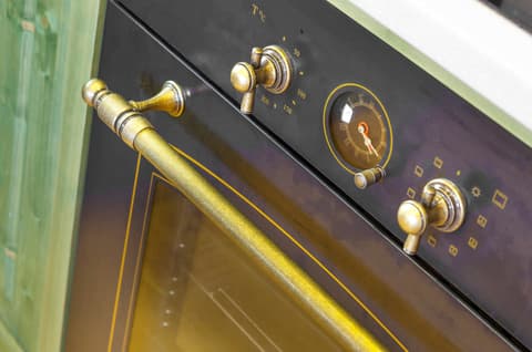 Detailní záběr na ovládací prvky a design retro vestavné trouby v rustikální kuchyni.